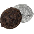 Round dark brown tea cake next to a piece of silver foil on a white background

