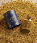 Two containers on a bed of yellow seeds, one blue and one glass with wooden cap.

