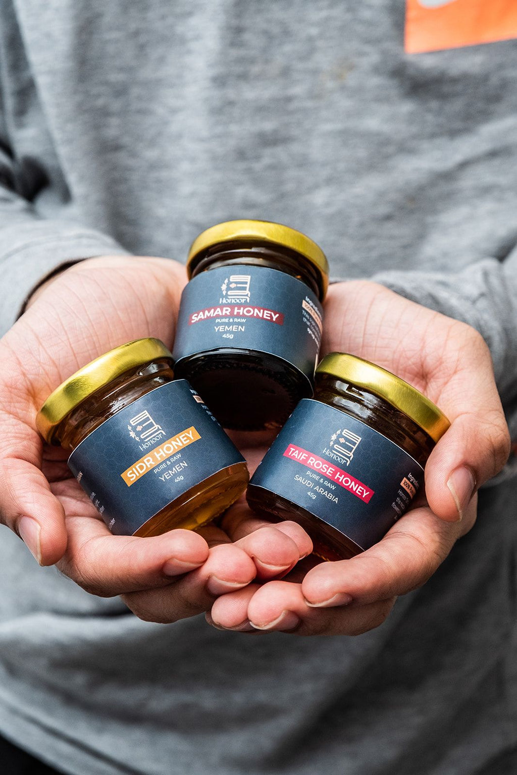 Three jars of Damar Honey held in hands against a gray background

