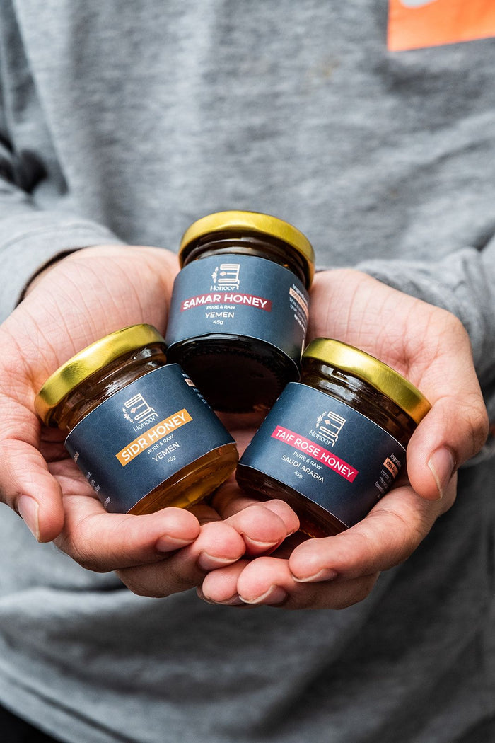 Three jars of Damar Honey held in hands against a gray background

