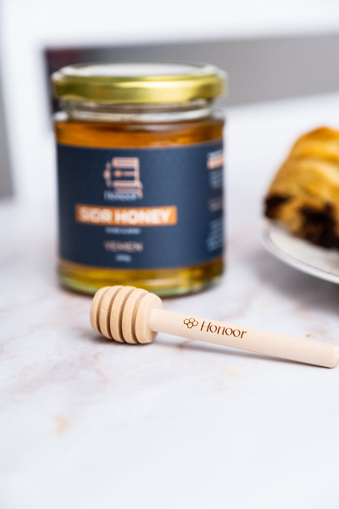 Jar of honey with a honey dipper on a marble surface


