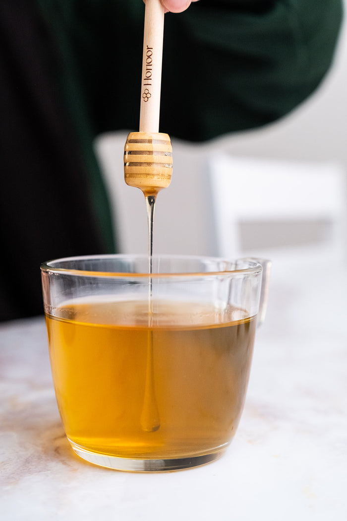 Honey being drizzled into a glass of tea using a wooden honey dipper.

