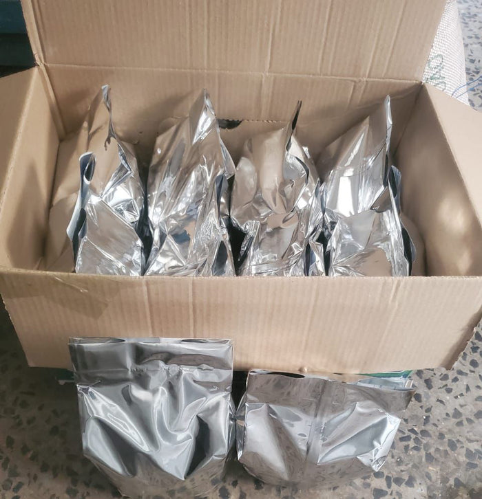 Cardboard box filled with silver foil packages on a textured surface.

