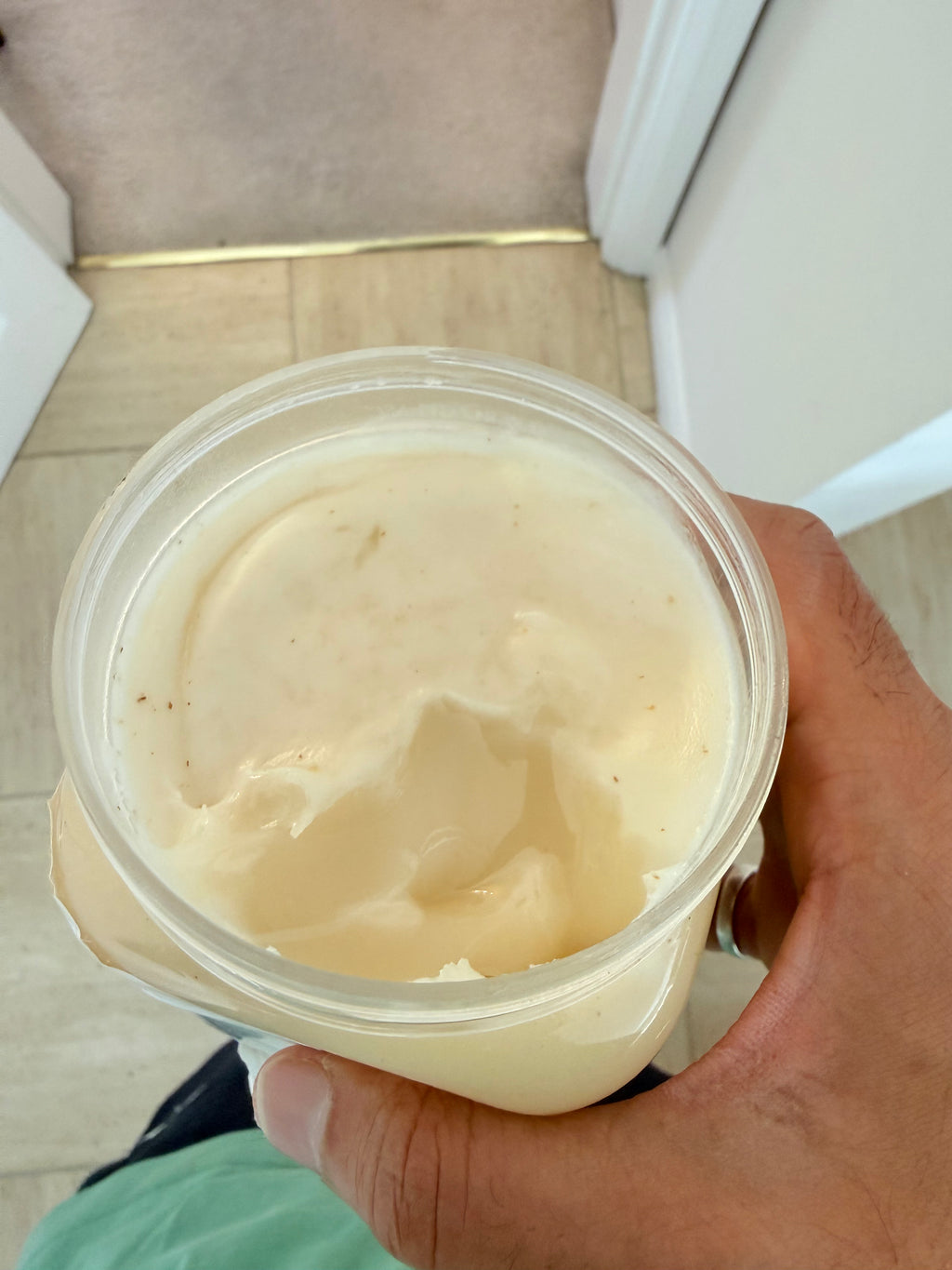 Hand holding a container of beige cream or yogurt indoors

