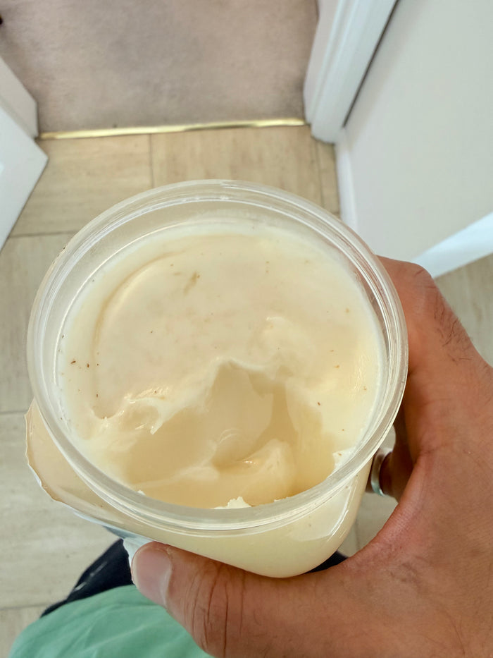 Hand holding a container of beige cream or yogurt indoors

