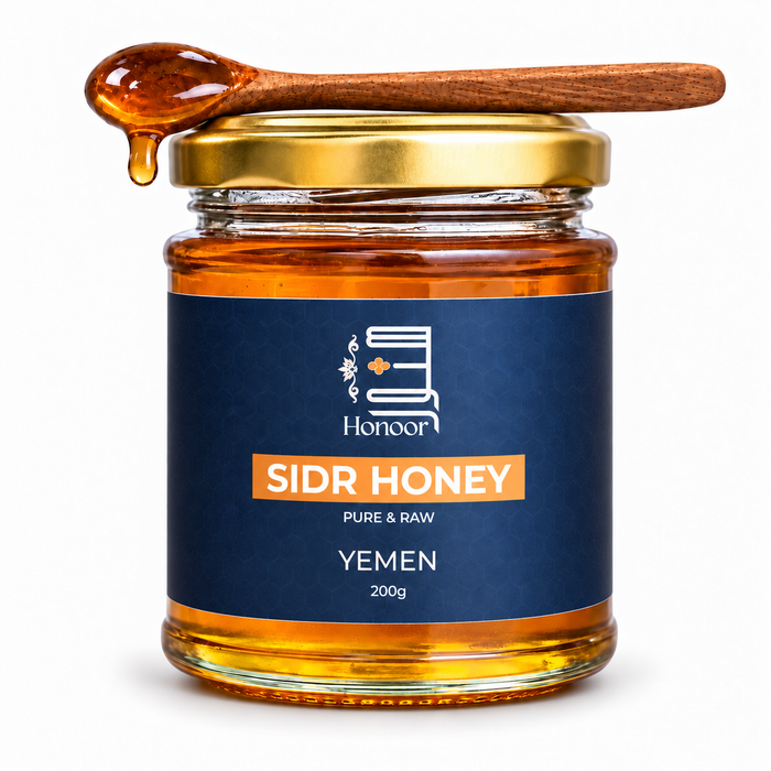 A glass jar of Sidr Honey from the brand Honoor, featuring a dark blue label and a gold metal lid. A wooden spoon filled with dripping amber honey rests on top of the jar against a clean white background.

