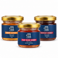 Three glass jars of honey with gold lids and blue labels are arranged on a white background. The center jar is labeled Taif Rose Honey, while the side jars are labeled Sidr Honey and Samar Honey.