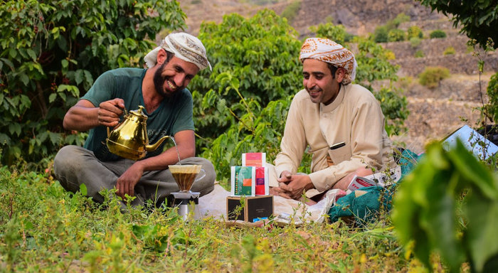 Two men sitting in a coffee plantation with coffee-related items.

