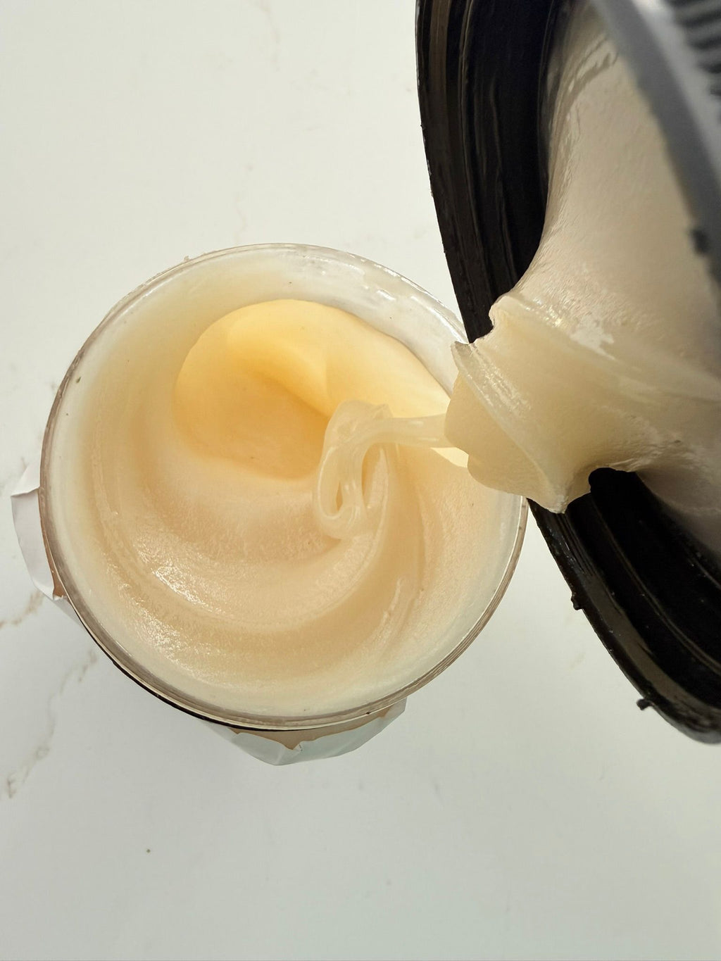 Cream being poured from a container into another container on a white background

