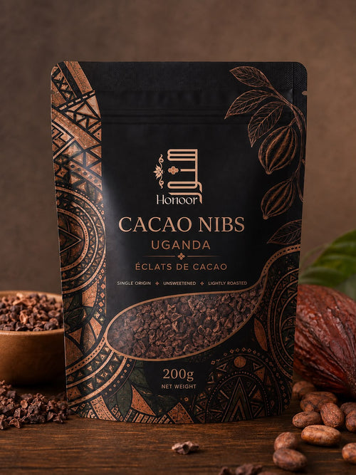 A 200g stand-up pouch of Honoor Cacao Nibs Uganda, featuring a black and bronze geometric design with a clear window showing roasted cacao nibs inside. The pouch is styled on a wooden surface with cacao beans, a bowl of cacao nibs, and a cacao pod in the background.

