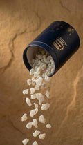 Container of white resinous substance spilling out on a sandy background

