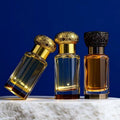 Three perfume bottles with gold, black, and brown caps on a textured surface with a blue background

