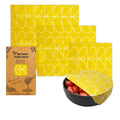 Yellow patterned beeswax food wrap with packaging and a bowl of tomatoes on a white background

